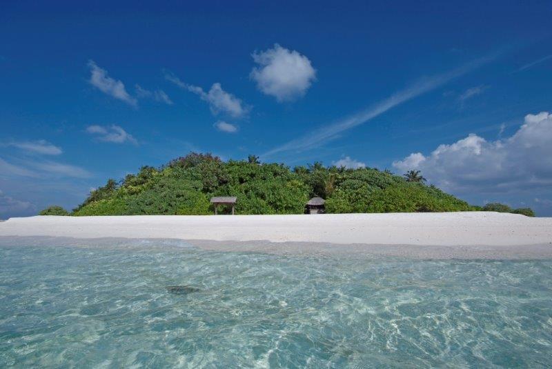 Skats no okeāna uz Makunudu Island kūrorta salu ar blīvu tropu veģetāciju un dzidru, seklu ūdeni priekšplānā