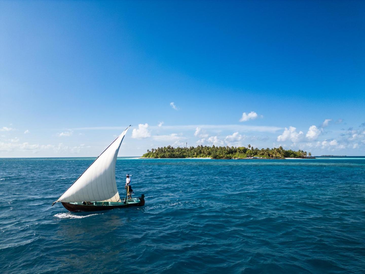 Tradicionālā Maldīvu dhoni laiva ar baltu buru zilajos Indijas okeāna ūdeņos pie Makunudu Island salas