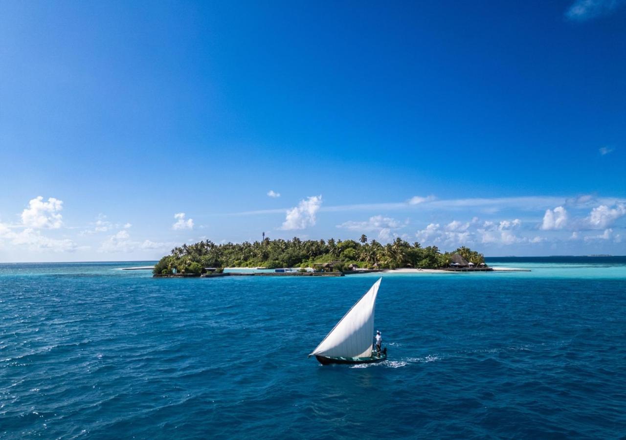 Tradicionāla buru laiva okeānā pie Makunudu Island kūrorta Maldīvās — skats uz tropu salu ar palmām no tālienes