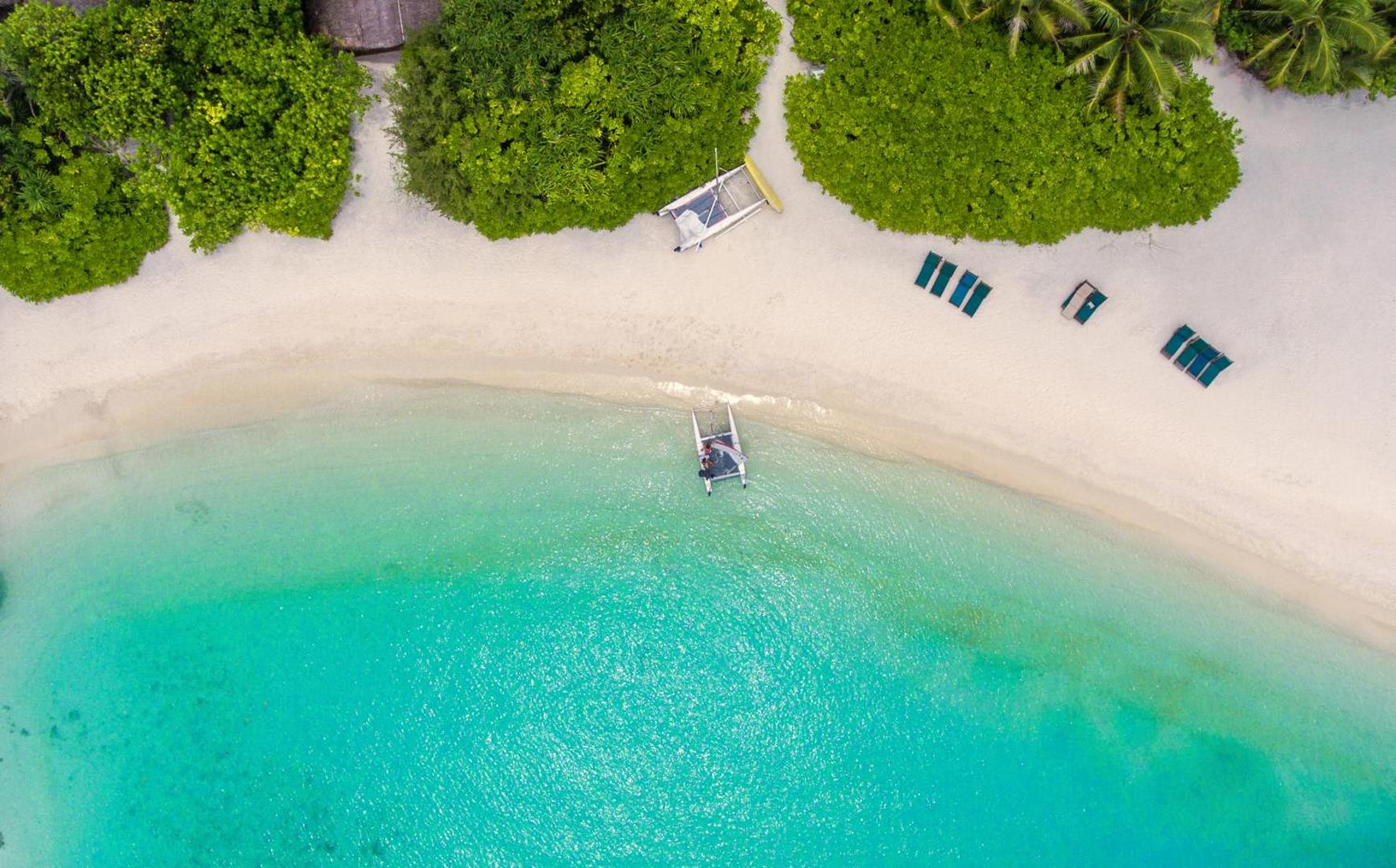Makunudu Island aerofoto skats uz tirkīza lagūnu un balto smilšu pludmali Maldīvās ar nelielu buru laivu krastā