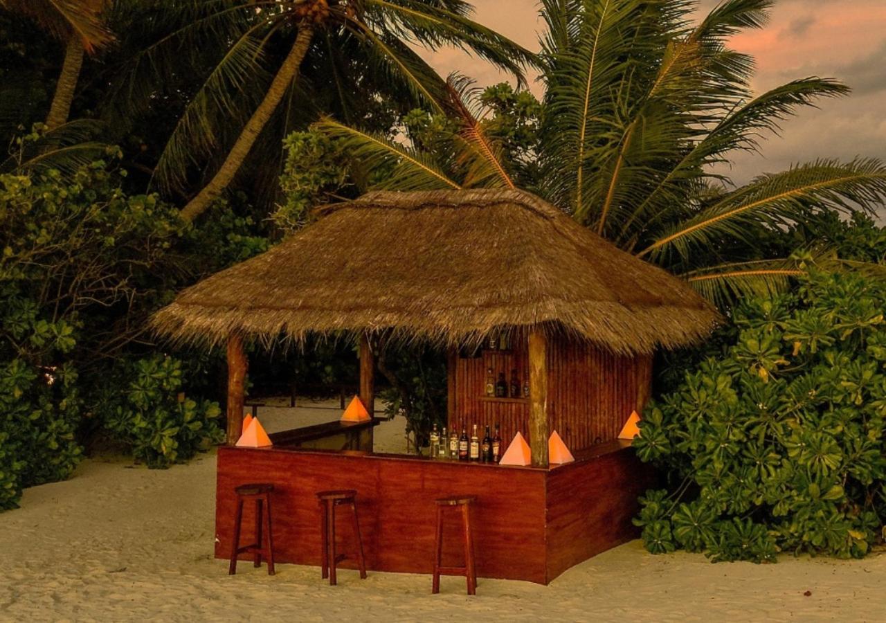 Makunudu Island pludmales bārs ar niedru jumtu un koka apdari saulrietā, ieskauts palmu un tropisko augu zaļumos