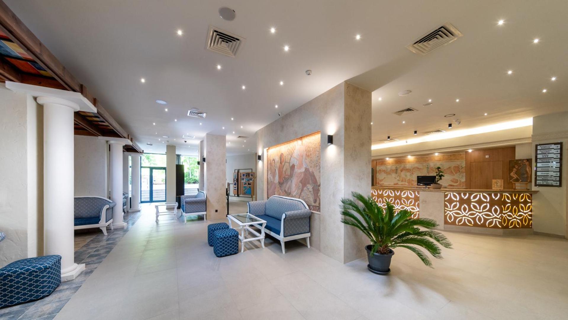 Viesnīcas Sentido Bellevue Beach lobby zona ar recepciju, atpūtas dīvāniem, kolonnām un dekoratīviem sienas gleznojumiem