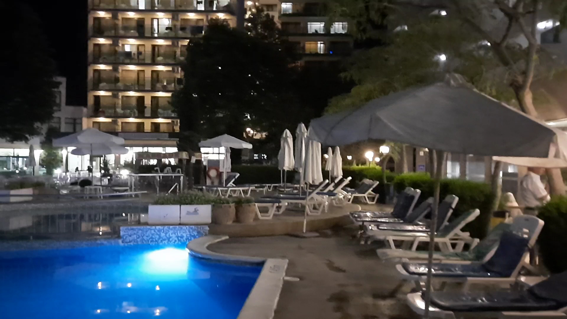 Sentido Bellevue Beach āra baseins vakarā ar zilu apgaismojumu, sauļošanās krēsliem un viesnīcas ēku fonā Saulainajā krastā, Bulgārijā
