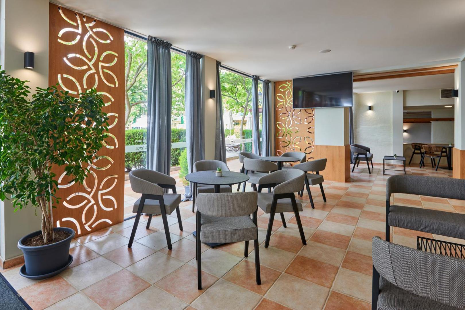 Sentido Bellevue Beach gaiša atpūtas telpa ar moderniem krēsliem, lieliem logiem un dekoratīviem koka paneļiem piekrastes viesnīcā
