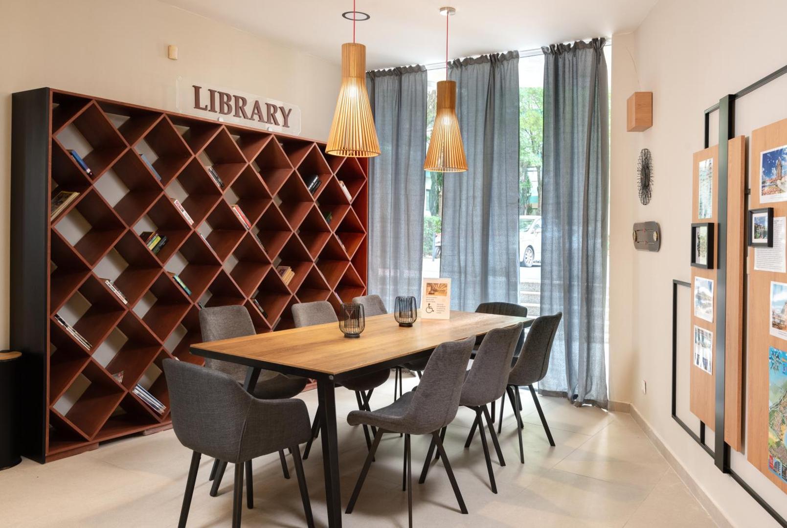 Sentido Bellevue Beach viesnīcas koplietošanas telpa ar bibliotēku, koka galdu un stilīgiem pelēkiem krēsliem atpūtai