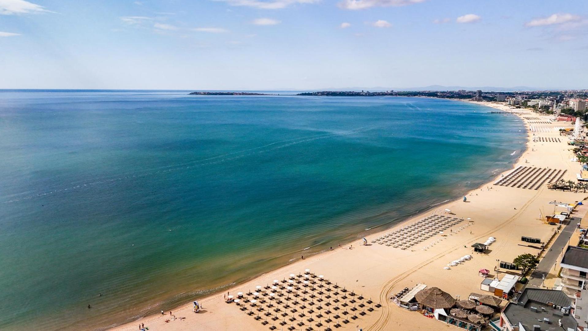 Aerofoto skats uz Sentido Bellevue Beach plašo smilšu pludmali un Melno jūru Saulainajā krastā ar saulessargu rindām