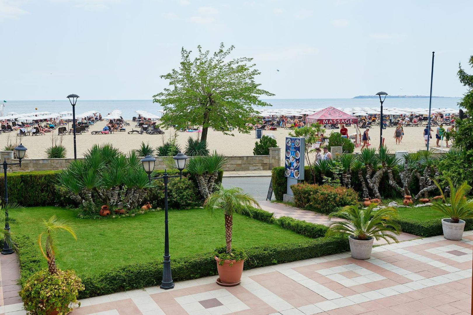 Skats no Sentido Bellevue Beach terases uz labiekārtotu dārzu un plašo smilšu pludmali ar saulessargiem Saulainajā krastā