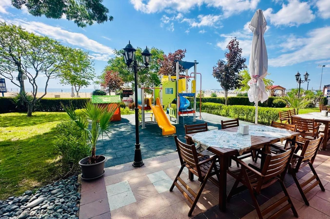 Sentido Bellevue Beach āra terase ar koka galdiem un skatu uz bērnu laukumu un jūras piekrasti Saulainajā krastā
