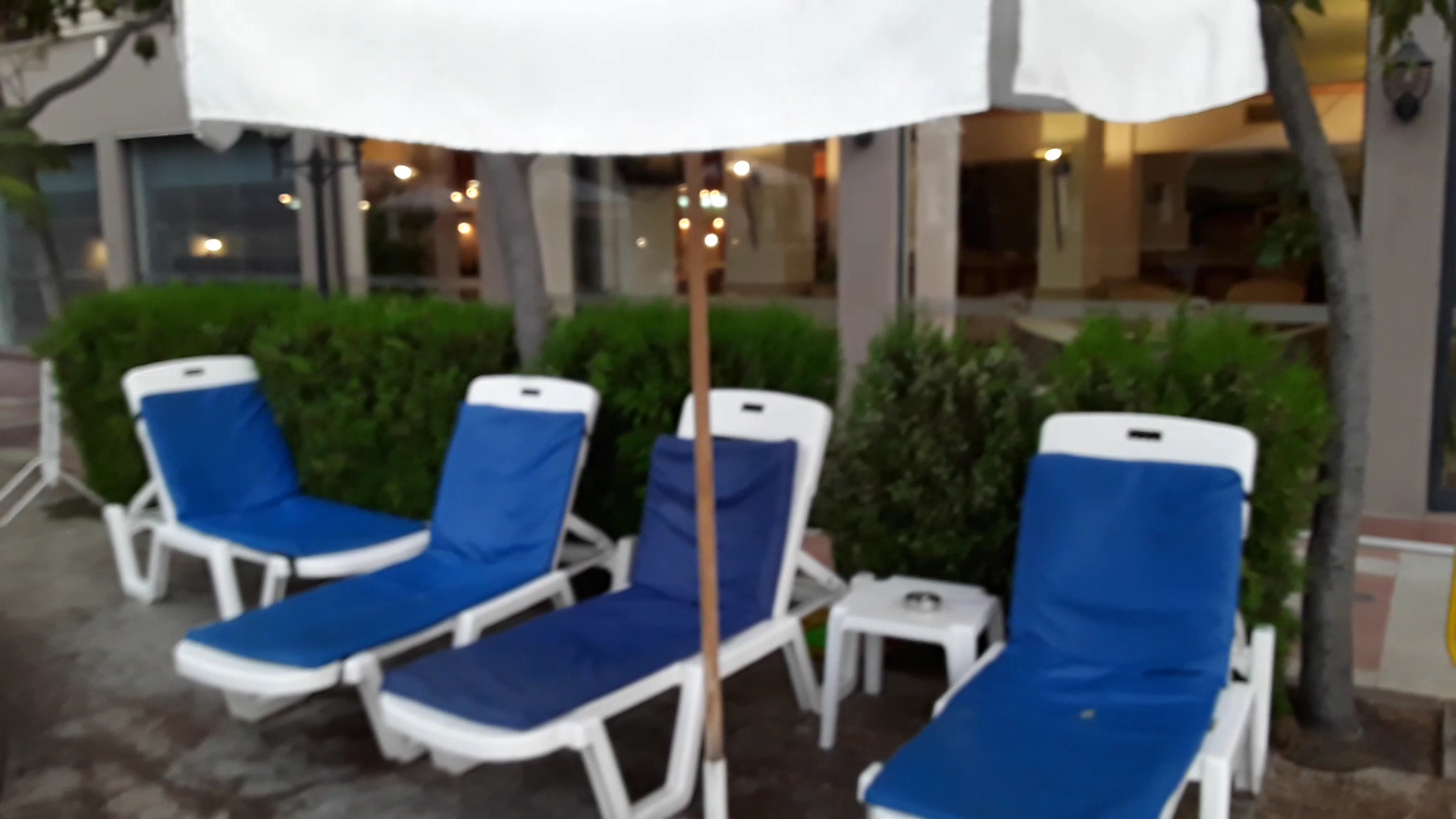 Zili sauļošanās krēsli zem saulessarga Sentido Bellevue Beach viesnīcas teritorijā, nodrošinot atpūtu pie baseina vai dārzā