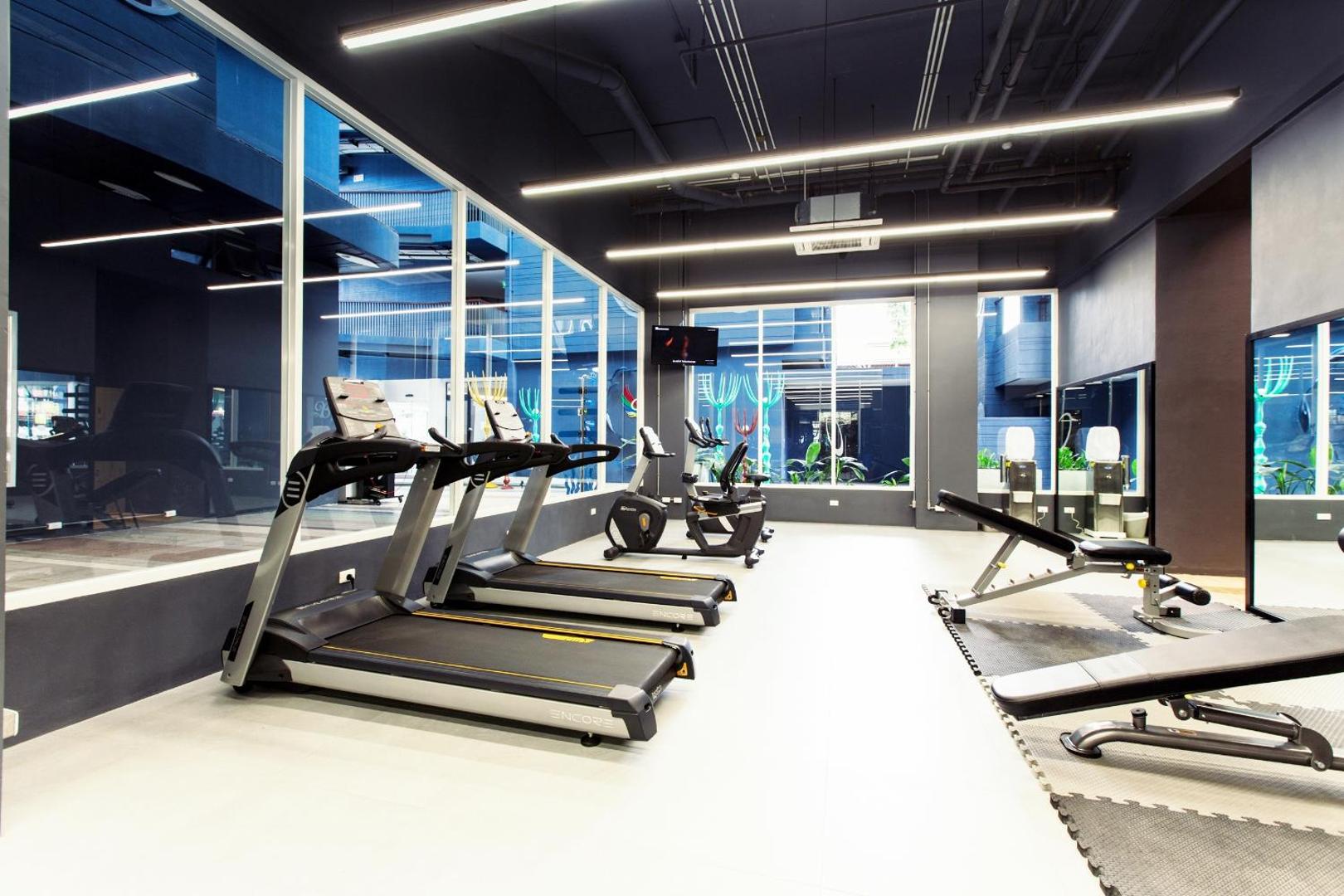 Beyond Patong fitnesa centrs ar skrejceliņiem un trenažieriem Puketā — gaiša sporta zāle ar lieliem logiem un modernu aprīkojumu