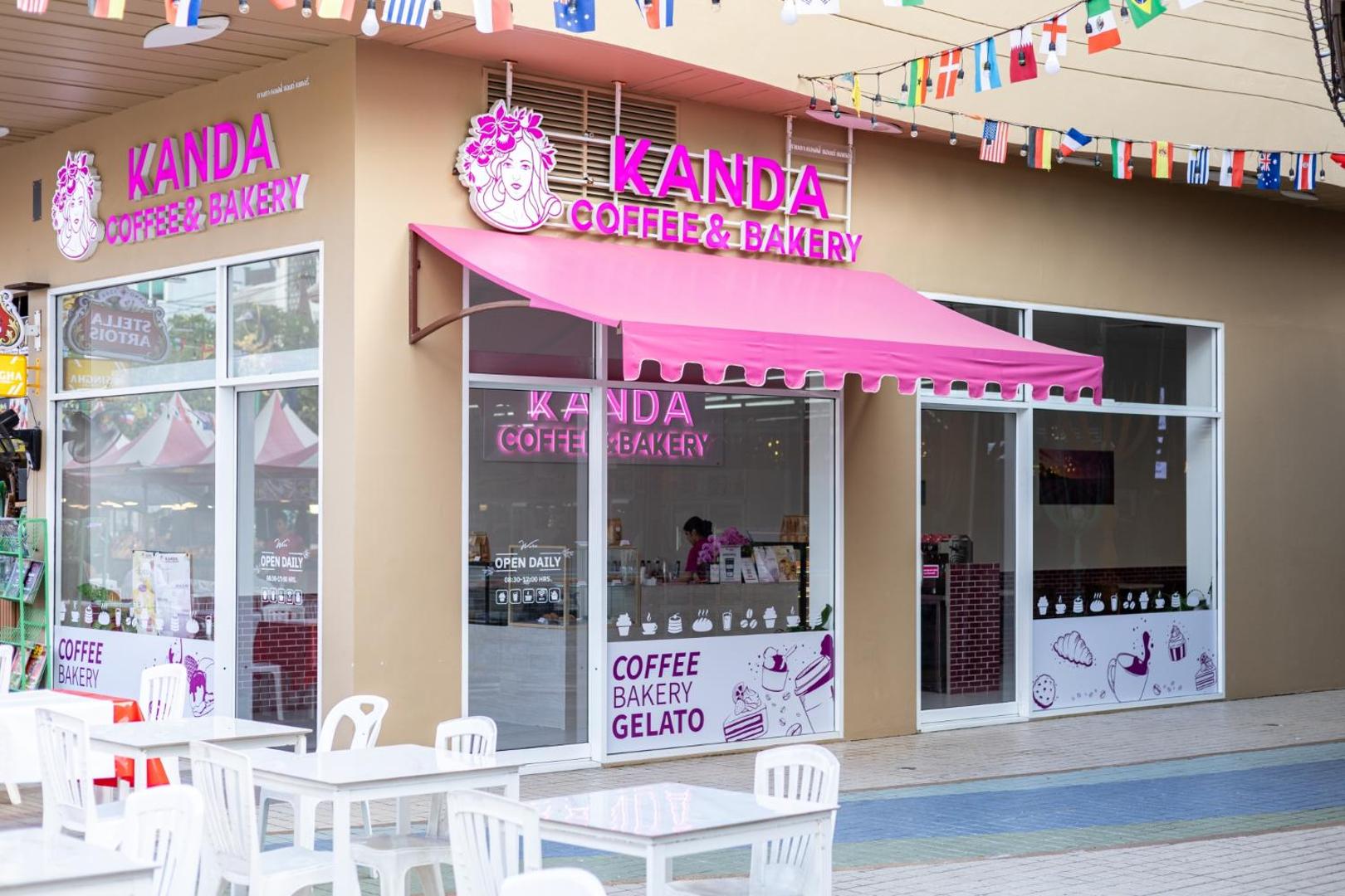 Kanda Coffee & Bakery ieeja pie Beyond Patong viesnīcas Puketā — rozā tentu nojume un balti āra galdiņi