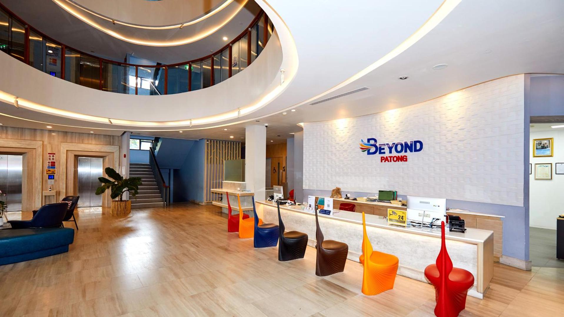 Beyond Patong viesnīcas modernā recepcija Puketā ar unikāla dizaina krāsainiem krēsliem, gaišu leti un plašu vestibila zonu