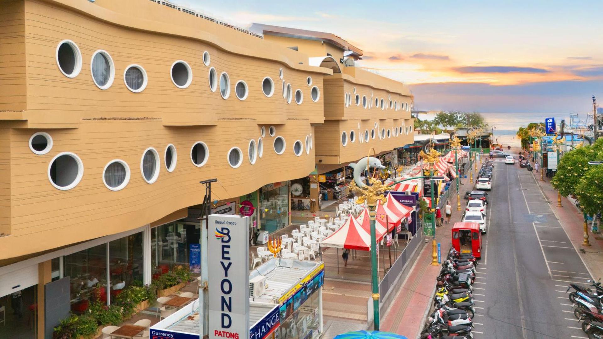 Beyond Patong viesnīcas fasāde ar apaļiem logiem un skatu uz ielu saulrietā Puketas salā, Taizemē — pilsētas ainava pie jūras
