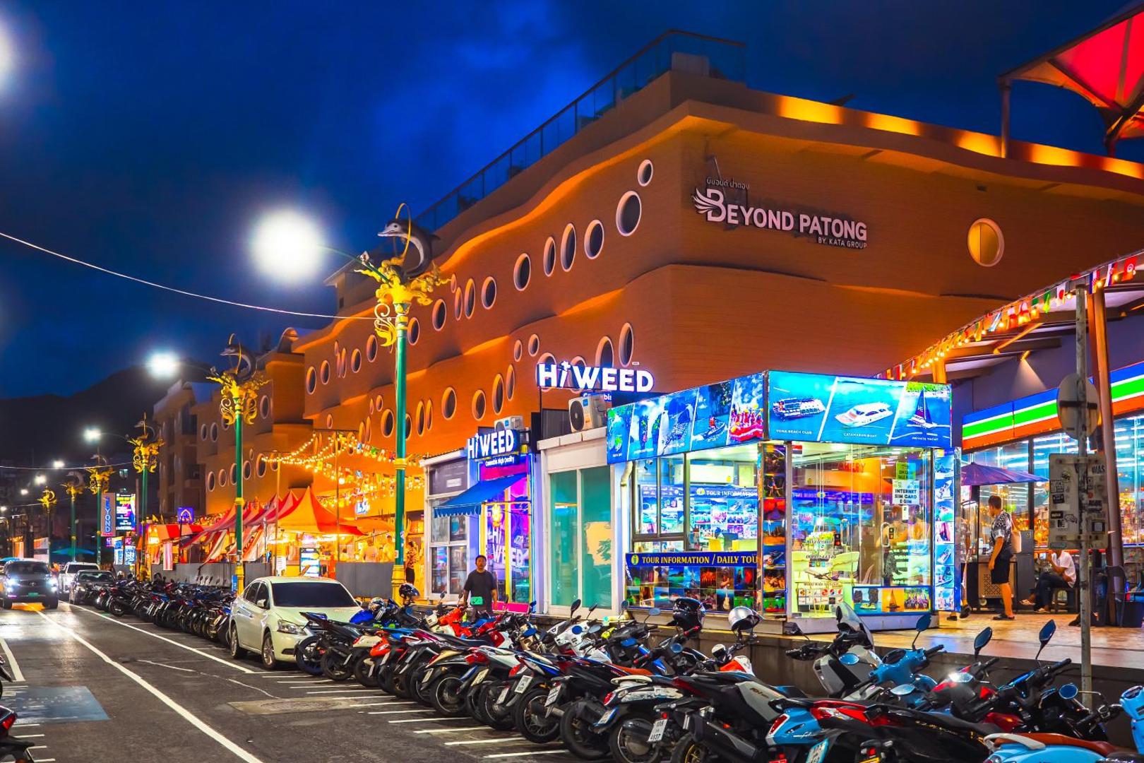 Beyond Patong viesnīcas ēka un apkārtne vakarā ar izgaismotām ielām un tūrisma informācijas punktu Puketā