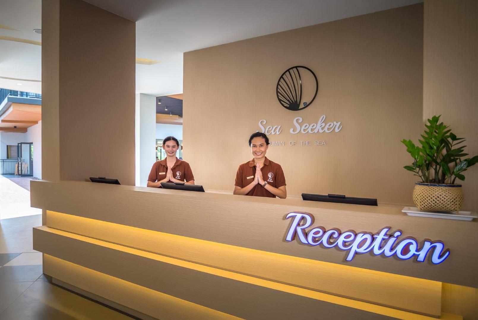 Sea Seeker Krabi Resort recepcijas zona ar smaidīgām darbiniecēm tradicionālā sveicienā pie gaiša koka reģistrācijas letes
