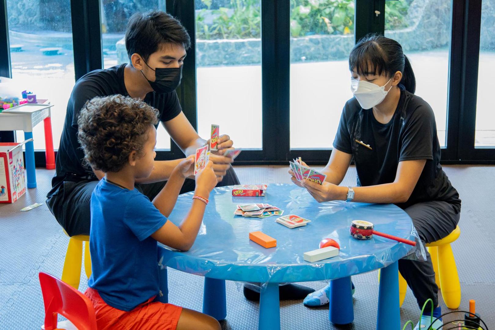 Sea Seeker Krabi Resort bērnu klubs ar rotaļu zonu, kur bērni un personāls pie galda spēlē galda spēles