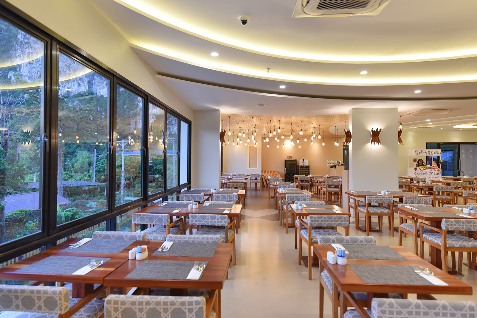 Sea Seeker Krabi Resort plašā restorāna zāle ar lieliem logiem, skatu uz kalniem un modernu apgaismojumu