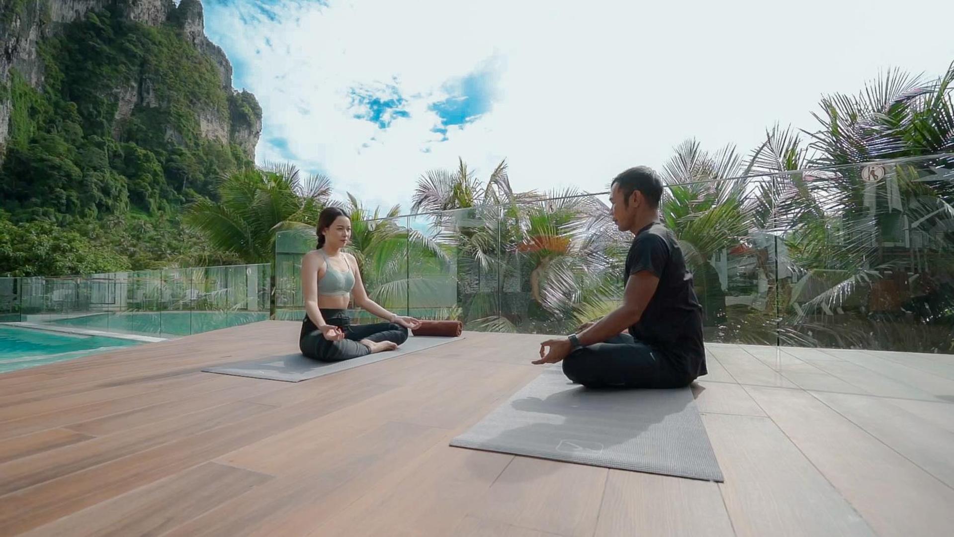 Jogas nodarbība uz Sea Seeker Krabi Resort āra terases ar skatu uz iespaidīgajām Krētas klintīm un palmām