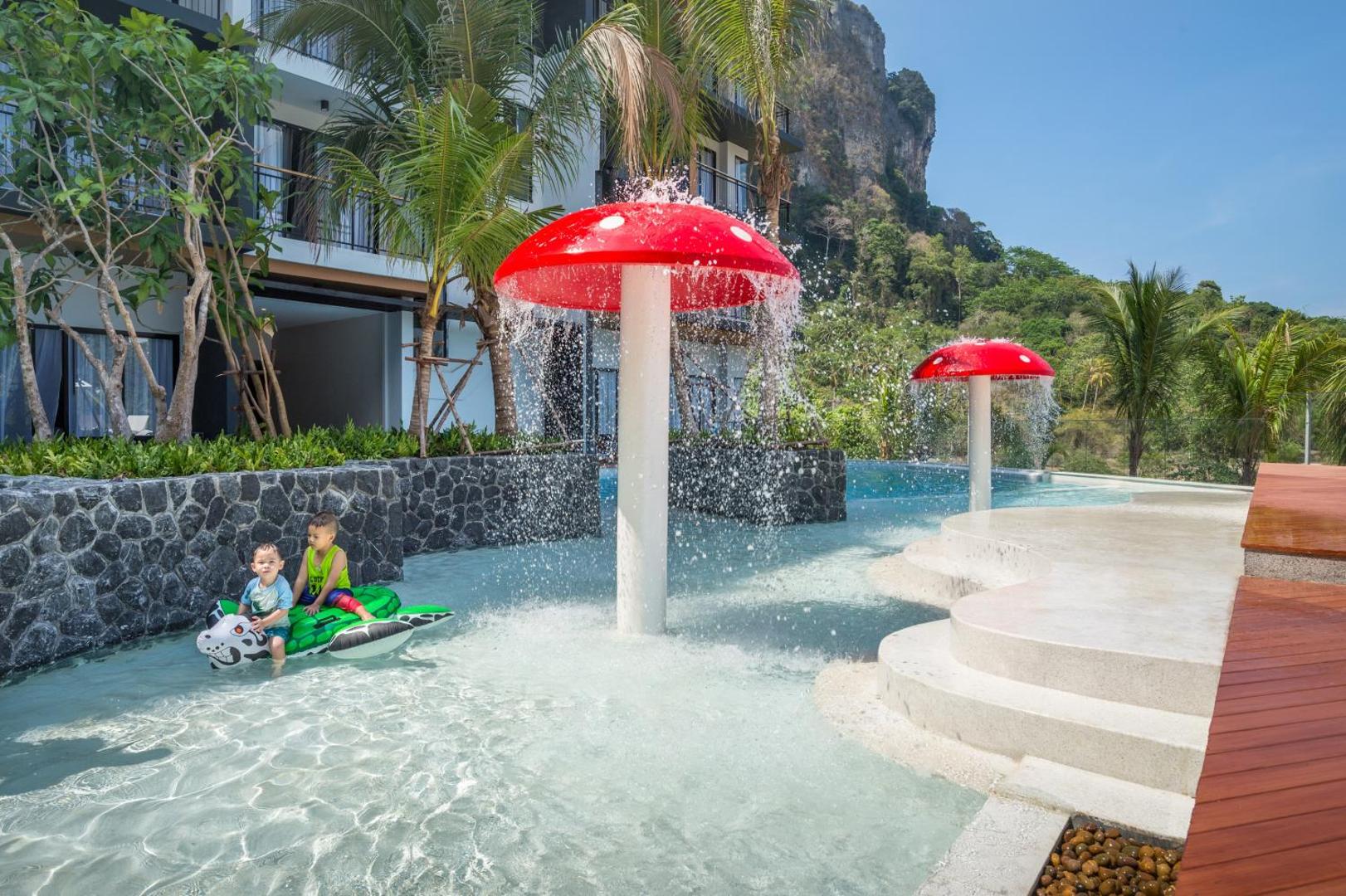 Bērnu baseins Sea Seeker Krabi Resort ar sēņu formas strūklakām un rotaļlietām — fonā redzami kalni un viesnīcas korpuss