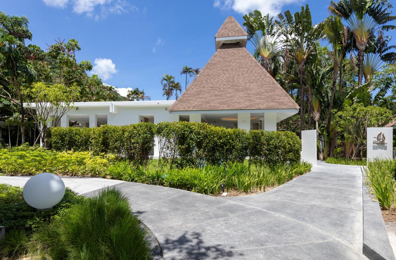 Centara Karon Resort Phuket spa centra ieeja ar raksturīgu piramīdas formas jumtu, ko ieskauj eksotiski augi un palmas Taizemes dārzā