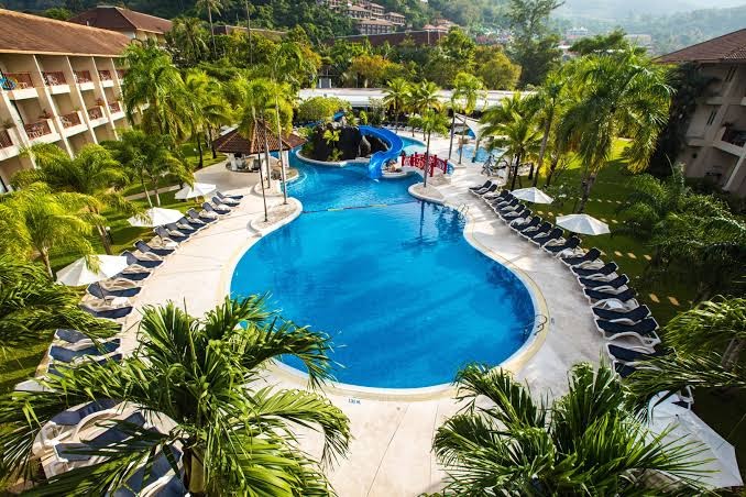 Centara Karon Resort Phuket lagūnas tipa baseins ar ūdens slidkalniņu, tiltiņu un daudziem sauļošanās krēsliem palmu ielenkumā