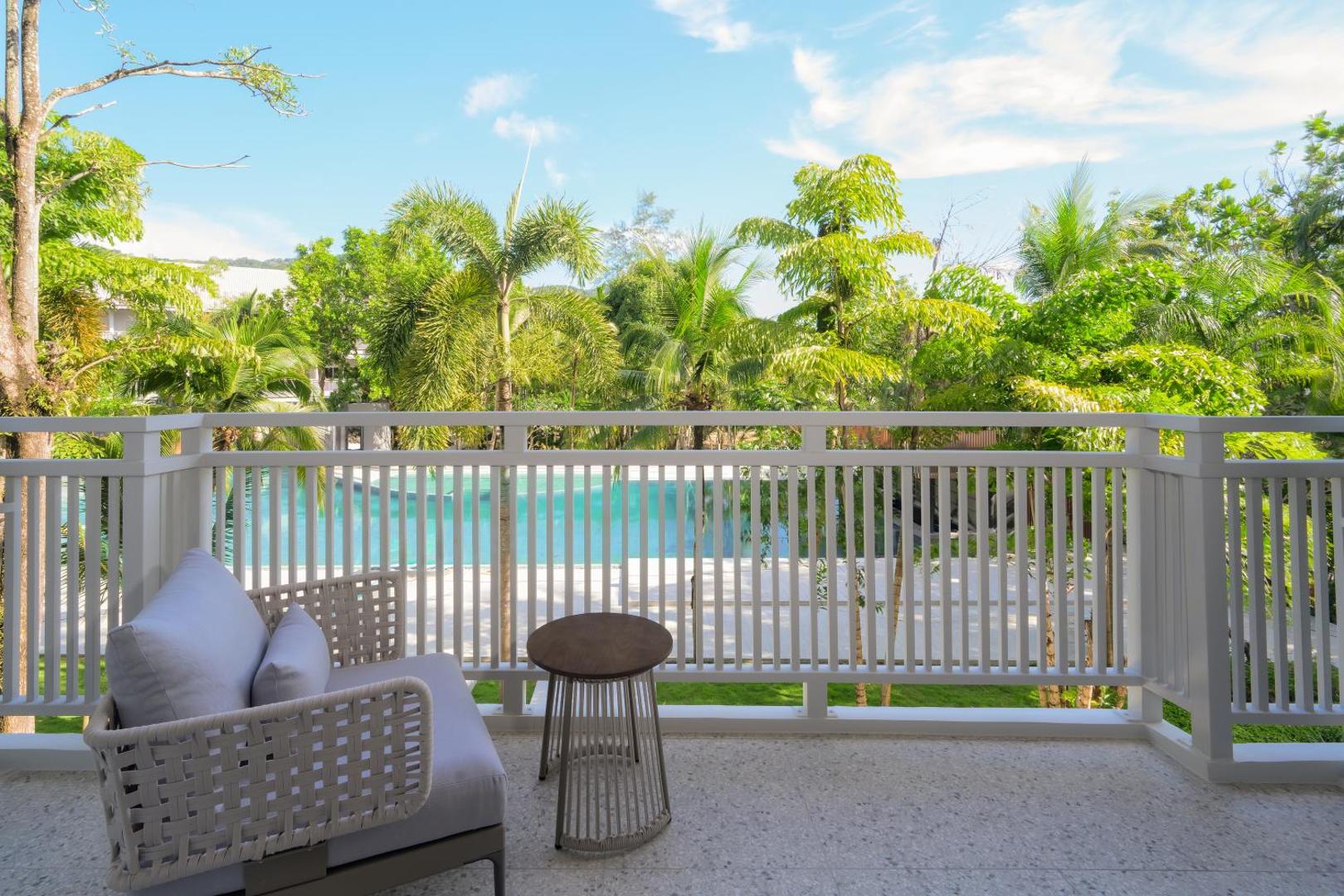 Centara Karon Resort Phuket numura balkons ar ērtu krēslu un skatu uz baseinu un palmām Puketas kūrortā