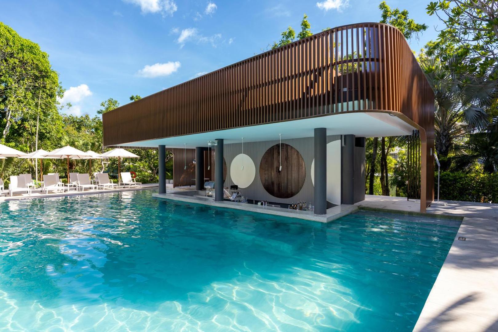 Centara Karon Resort Phuket moderns peldbaseins ar bāru ūdenī, ko ieskauj tropu dārzs un sauļošanās krēsli ar saulessargiem