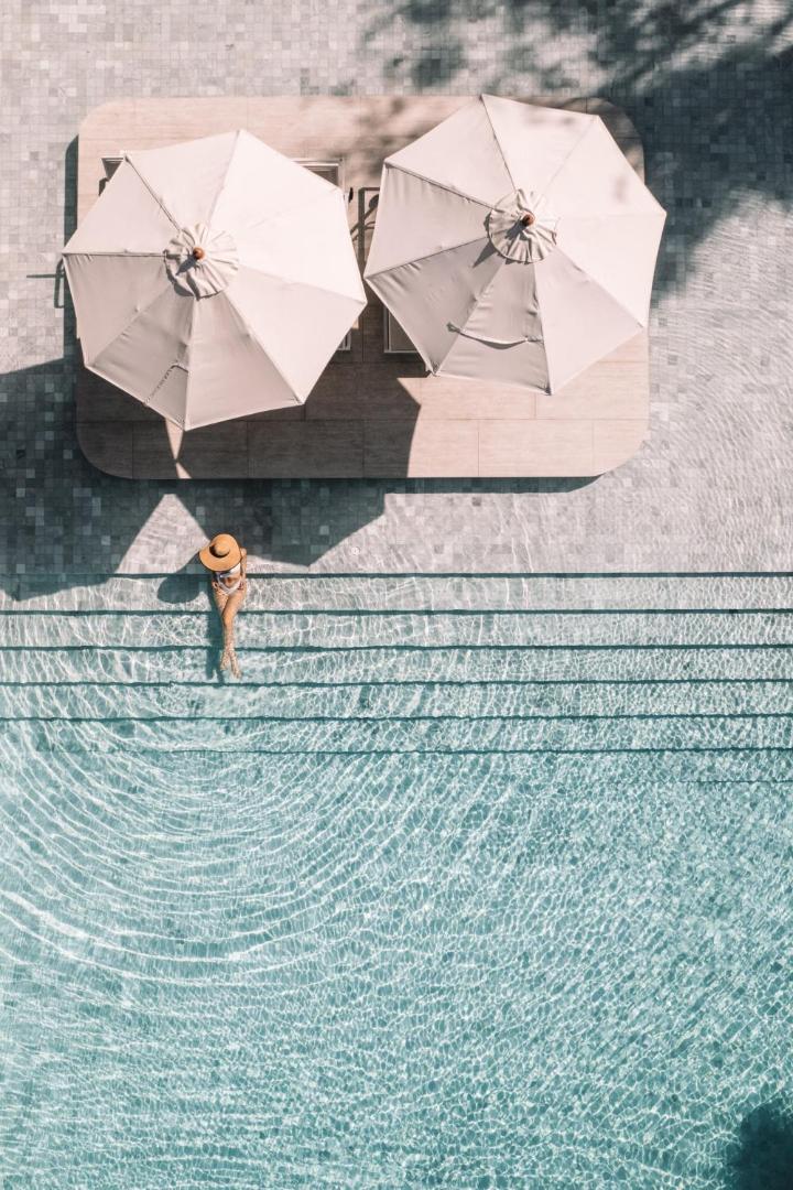 Skats no augšas uz sievieti cepurē pie Centara Karon Resort Phuket baseina malas zem gaišiem saulessargiem
