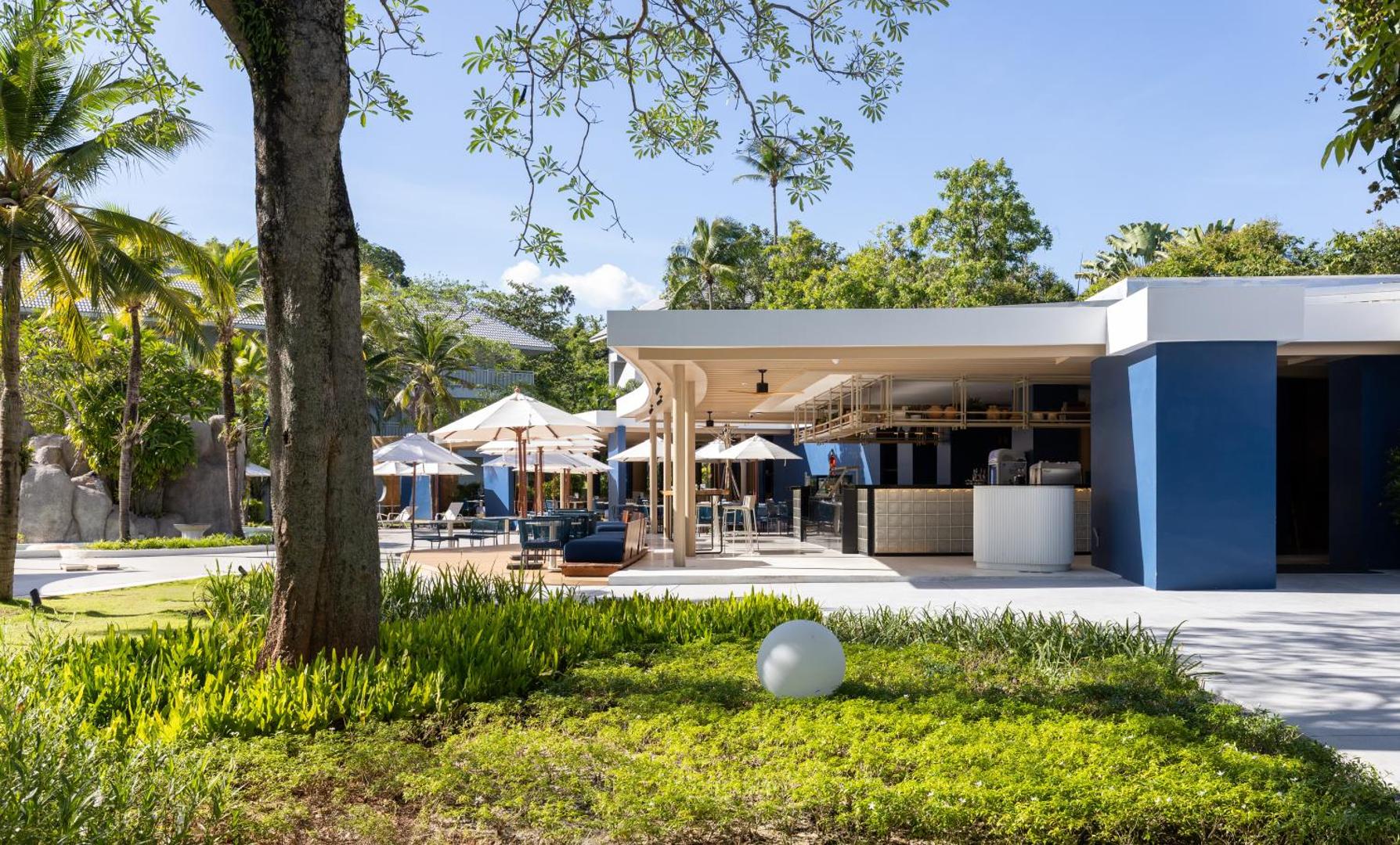 Centara Karon Resort Phuket āra bārs un atpūtas zona ar ziliem akcentiem, saulessargiem un tropu dārzu Puketā, Taizemē