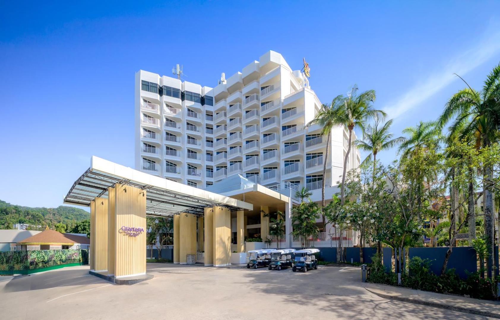 Centara Karon Resort Phuket galvenā ēka ar modernu arhitektūru, balkoniem un palmu dārzu pie ieejas, kur novietoti golfa kapiņi