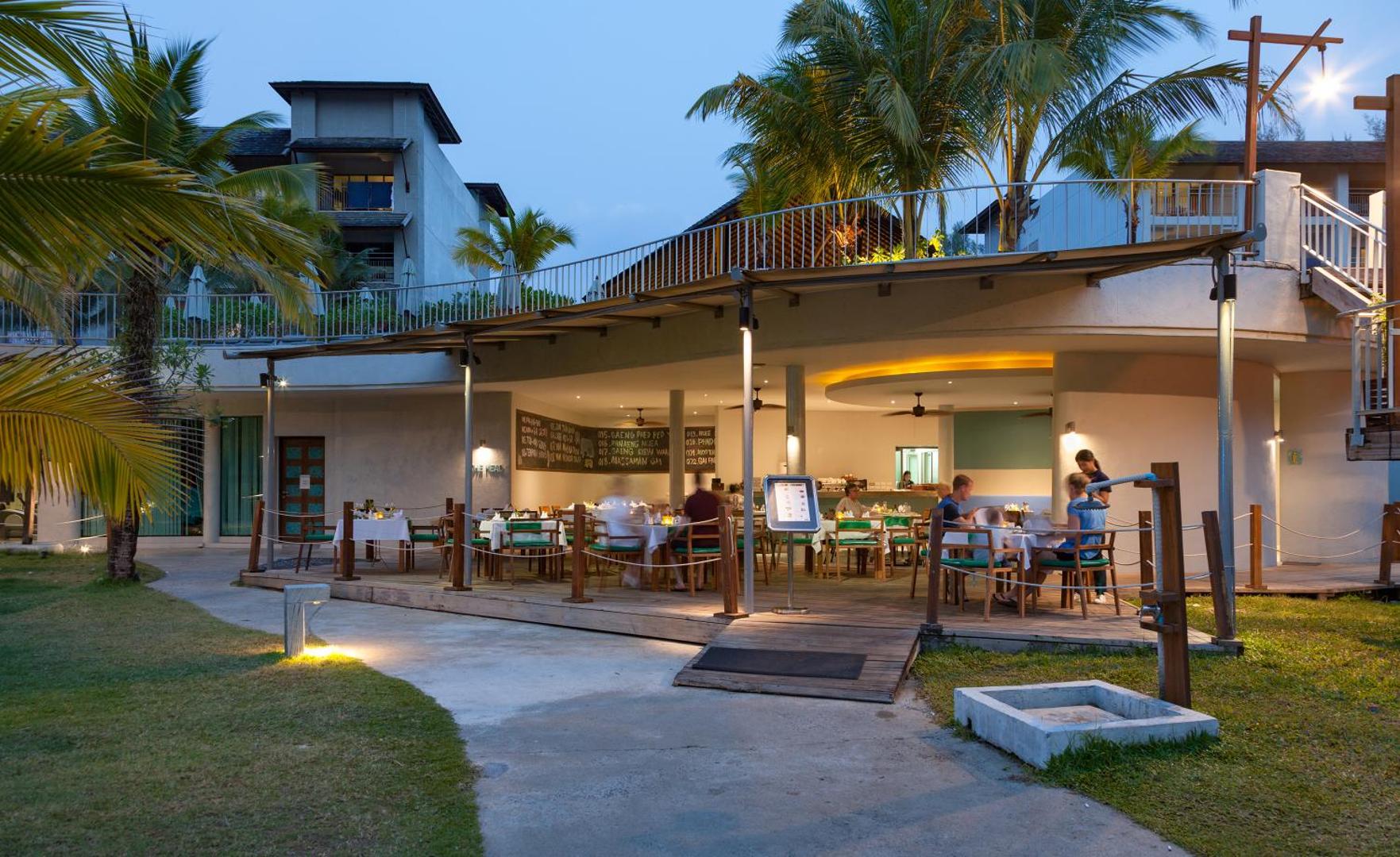 Mai Khao Lak Beach Resort & Spa vakara apgaismojums āra restorāna terasē ar skatu uz kūrorta ēkām un palmām
