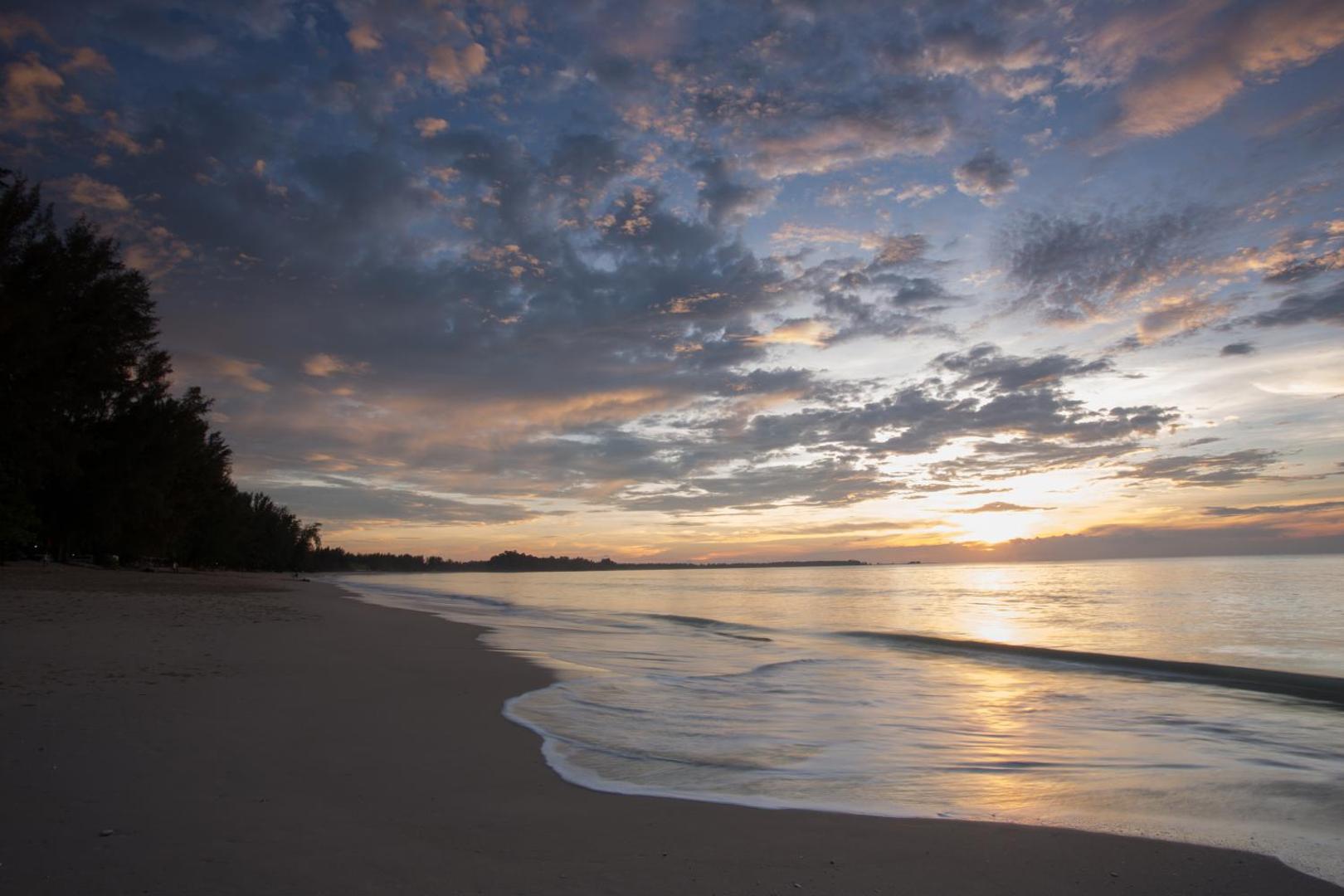 Saulriets Mai Khao pludmalē pie viesnīcas Mai Khao Lak Beach Resort & Spa — mierīga jūra un mākoņainas debesis