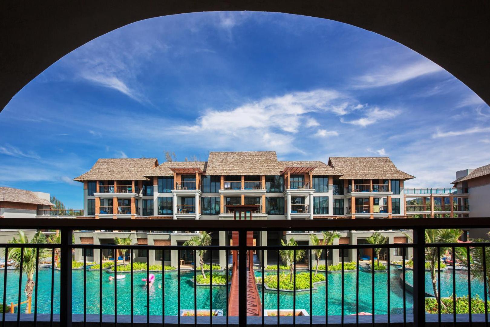 Skats no Mai Khao Lak Beach Resort balkona uz zilo baseinu un viesnīcas korpusiem caur dekoratīvu arku