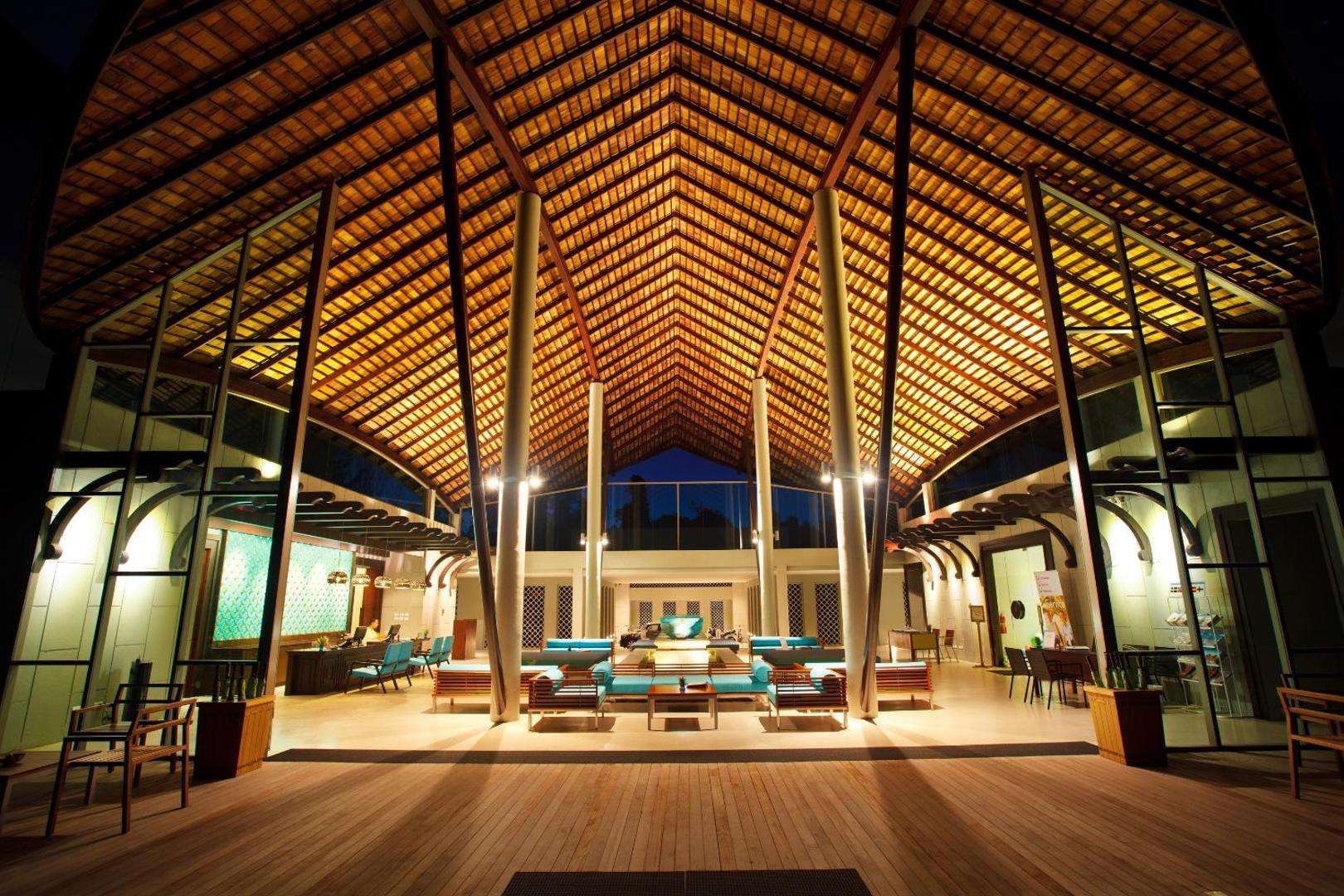Mai Khao Lak Beach Resort & Spa lobby vakara apgaismojumā ar augstiem koka griestiem un modernām mēbelēm