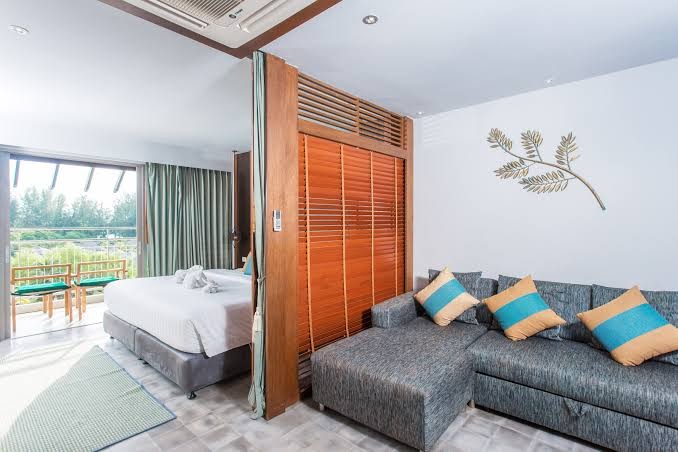 Gaišs viesnīcas numurs ar atsevišķu atpūtas zonu, pelēku dīvānu un skatu uz balkonu Mai Khao Lak Beach Resort & Spa