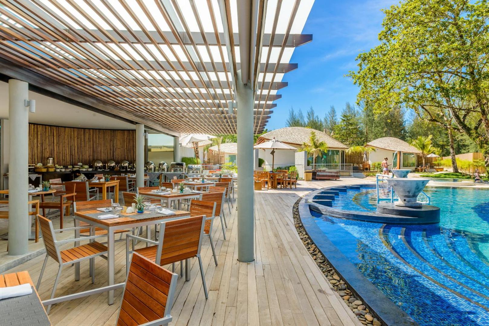 Mai Khao Lak Beach Resort & Spa āra restorāna terase pie baseina ar koka galdiem un saulessargiem Taizemes kūrortā