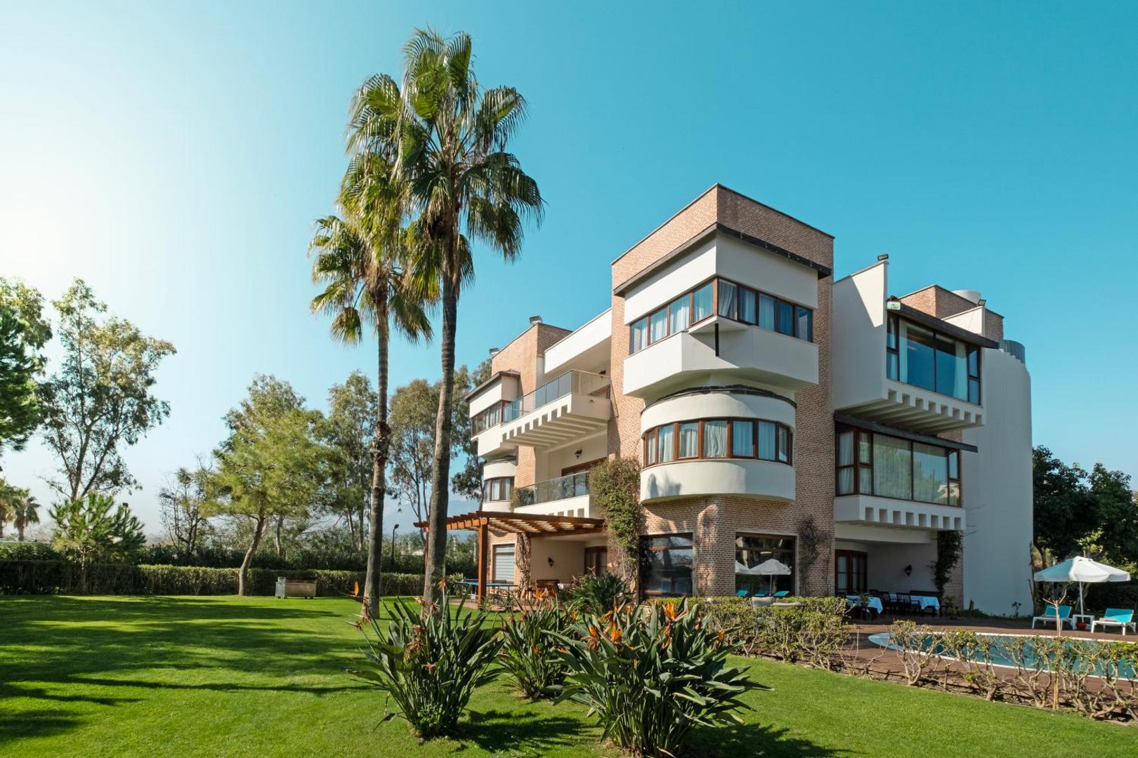 Limak Limra Hotel & Resort modernā arhitektūra un kopts zāliens ar palmām saulainā dienā Kemeras kūrortā