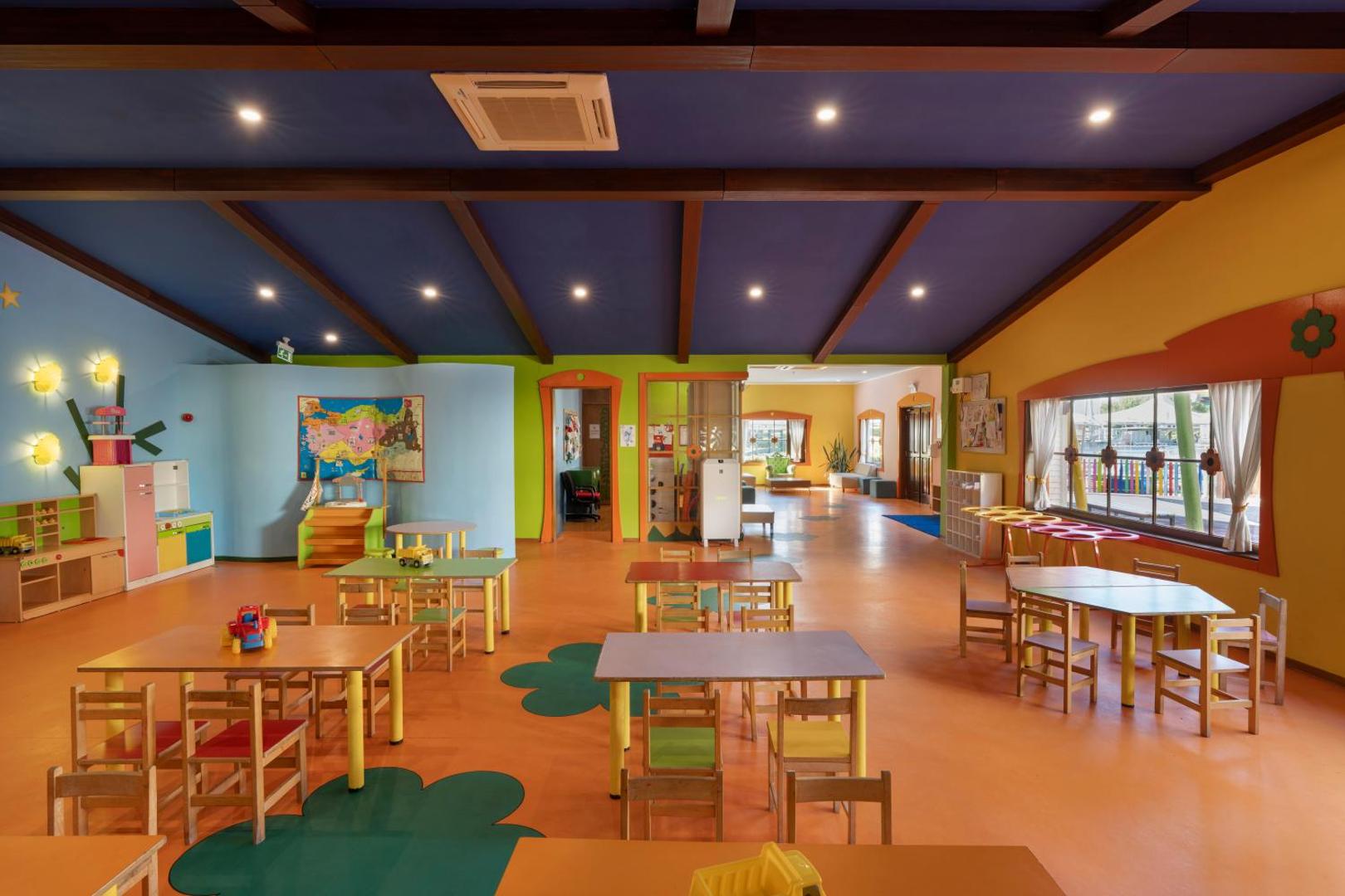 Limak Limra Hotel & Resort bērnu klubs ar krāsainiem galdiņiem, krēsliem un rotaļu zonu plašā, gaišā telpā