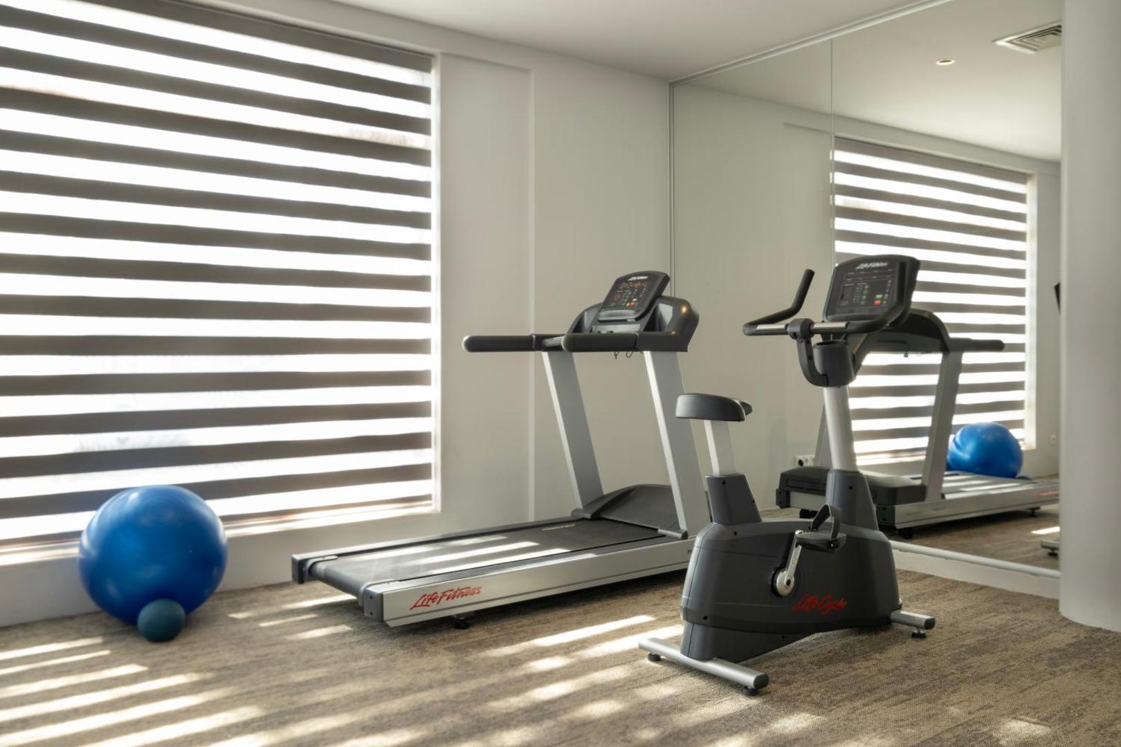Limak Limra Hotel & Resort fitness centrs ar skrejceliņu, velotrenažieri un lielu spoguli gaišā telpā