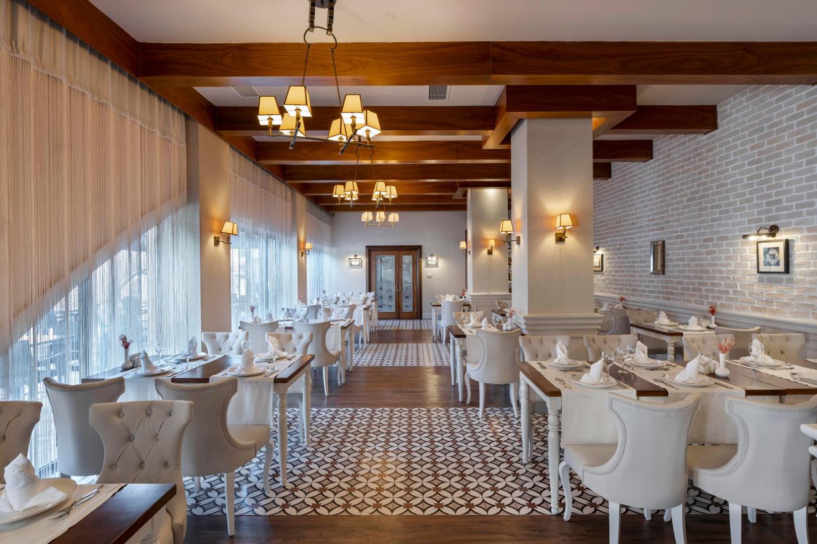 Limak Limra Hotel & Resort elegants restorāns ar baltiem krēsliem, koka griestu sijām un klasisku interjeru svinīgām vakariņām.