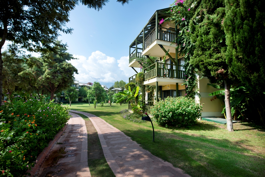 Limak Limra Hotel & Resort dārza mājiņas ar balkoniem un ziedošiem krūmiem pie gājēju celiņa Kirisā