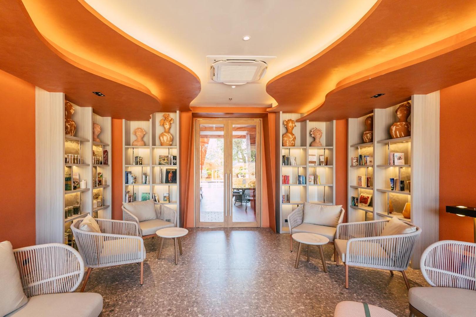 Hotel Adam Krabi atpūtas zona ar bibliotēku, ērtiem krēsliem un siltu apgaismojumu — mājīgs interjers ar mākslas elementiem