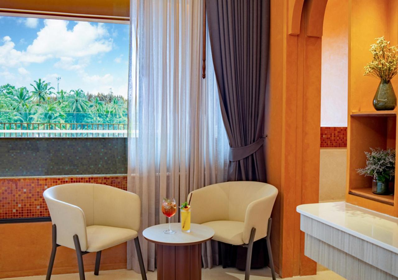 Atpūtas stūrītis Hotel Adam Krabi numurā ar diviem krēsliem, galdiņu un skatu uz palmu birzi caur logu