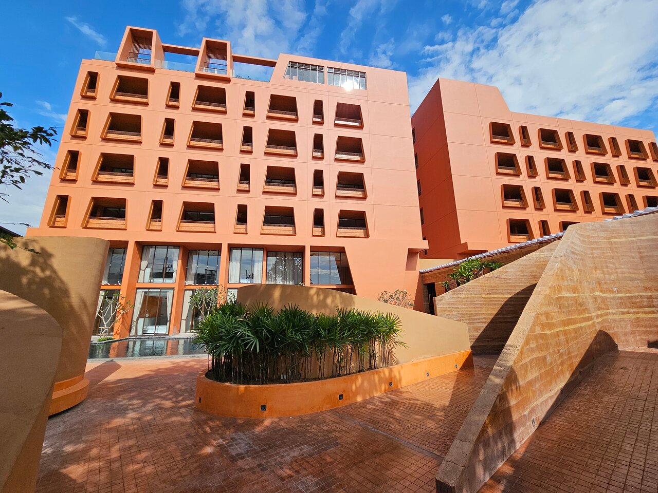 Hotel Adam Krabi iekšpagalms ar terakotas krāsas sienām un modernām kāpnēm zem skaidrām debesīm — skats uz viesnīcas numuru balkoniem