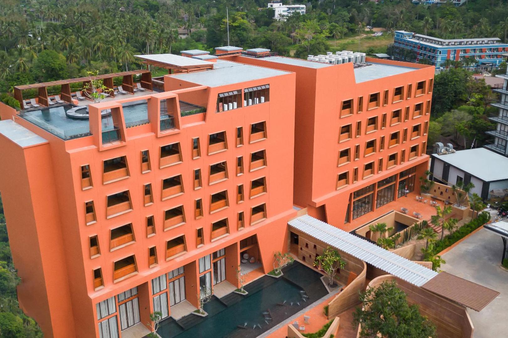 Hotel Adam Krabi mūsdienīgā oranžā ēka no putna lidojuma — redzams jumta baseins, sauļošanās terase un apkārtējie tropu zaļumi Krabi reģionā