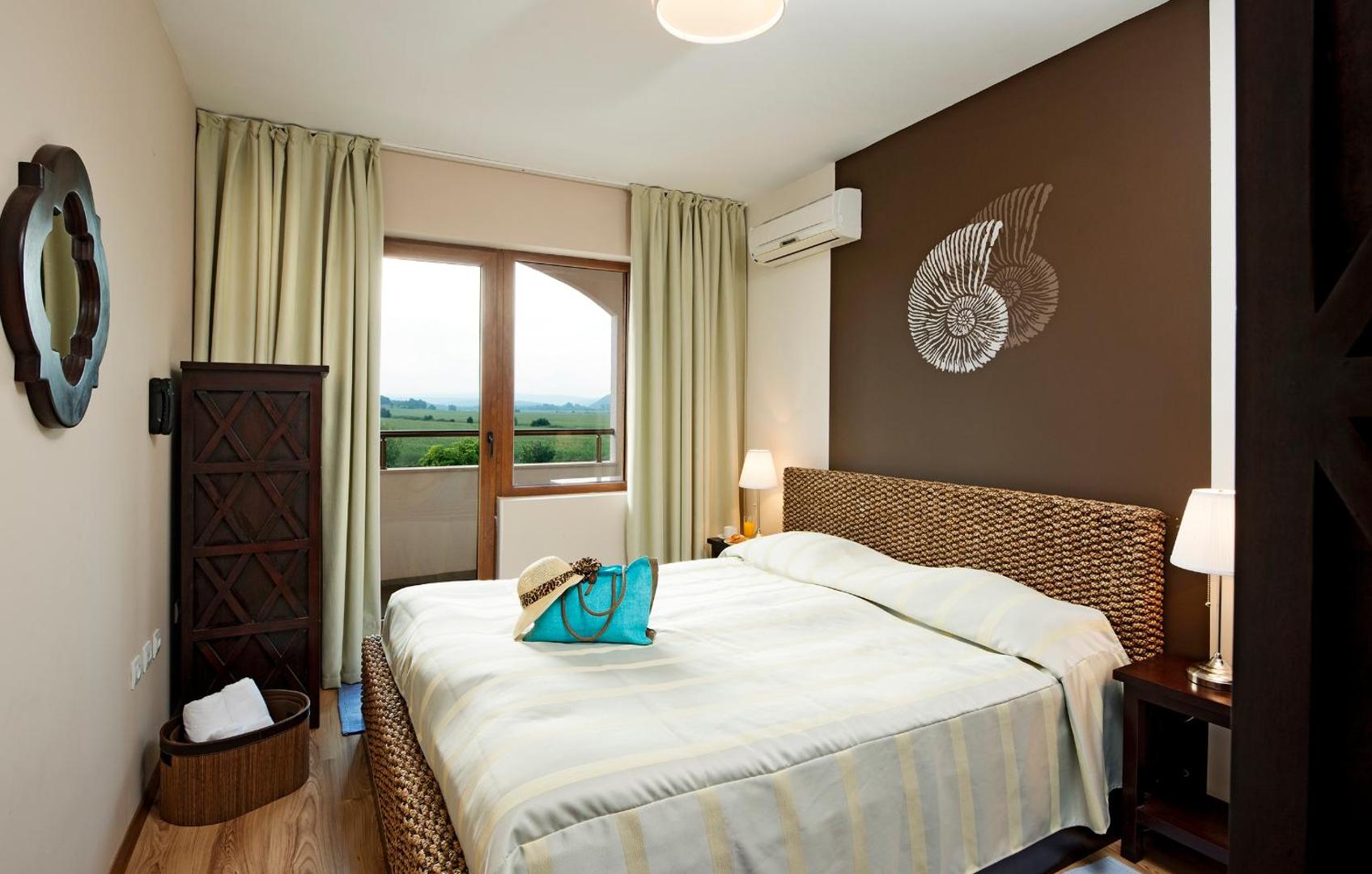 Sunrise All Suites Resort guļamistaba ar lielu gultu un balkonu — brūni interjera akcenti un skats uz zaļo apkārtni