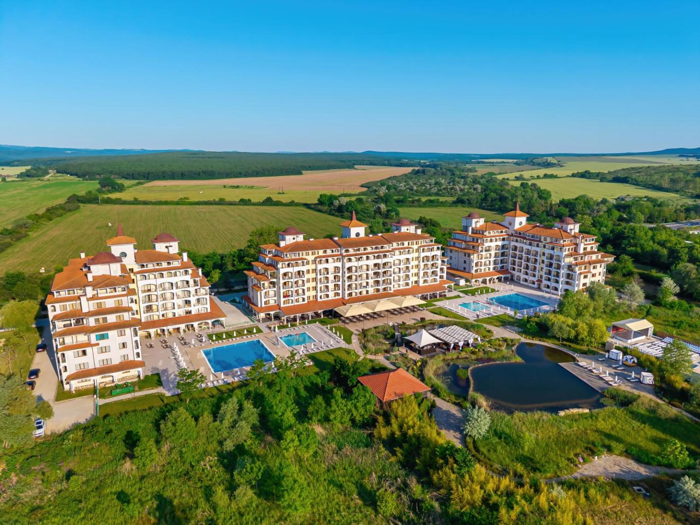 Sunrise All Suites Resort panorāmas skats no putna lidojuma Obzorā, Bulgārijā — viesnīcas korpusi, vairāki āra baseini un dīķis zaļā apkārtnē