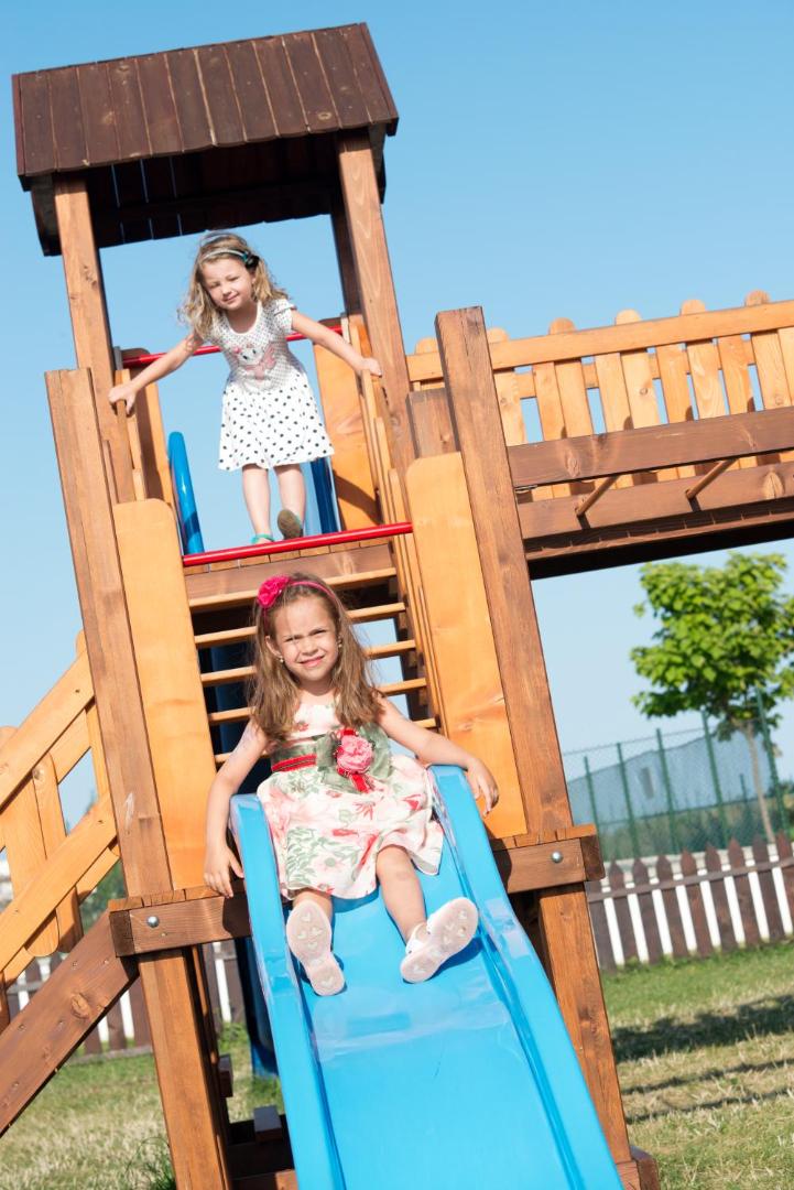 Divas meitenes spēlējas Sunrise All Suites Resort bērnu pilsētiņā, viena no viņām laižas lejā pa zilu slidkalniņu.