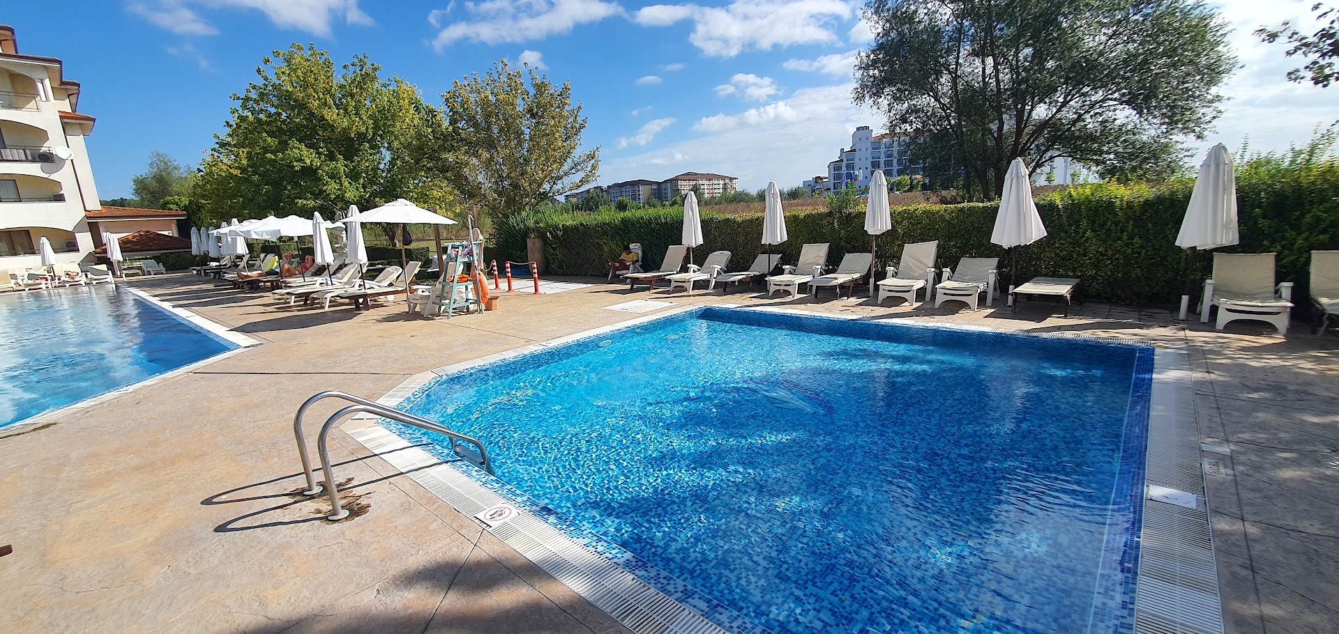 Sunrise All Suites Resort āra baseins ar dzidru ūdeni un sauļošanās krēsliem zem saulessargiem zaļumu ieskautā zonā