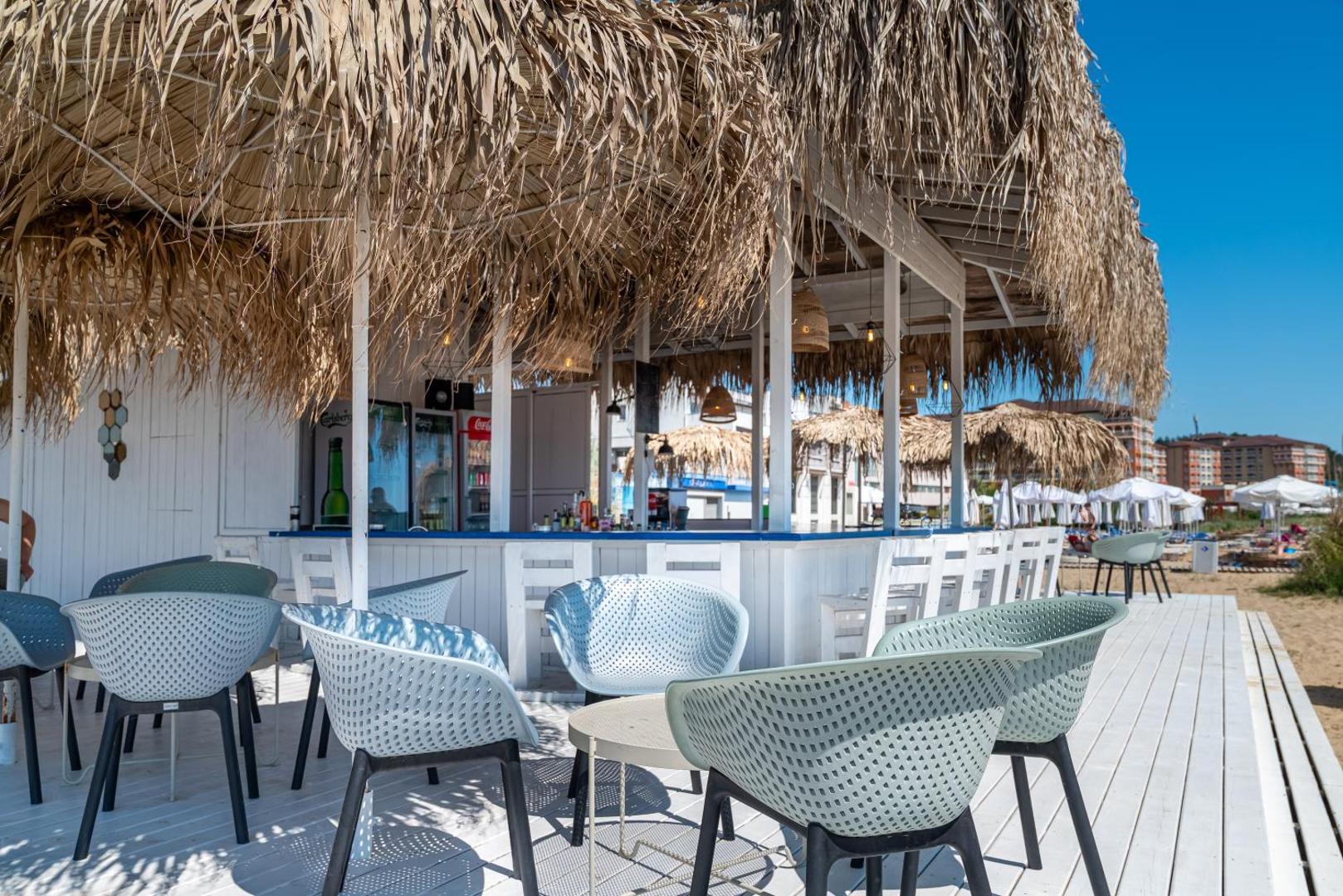 Sunrise All Suites Resort pludmales bārs ar salmu jumtu, stilīgiem krēsliem un gaišu koka terasi pašā jūras krastā